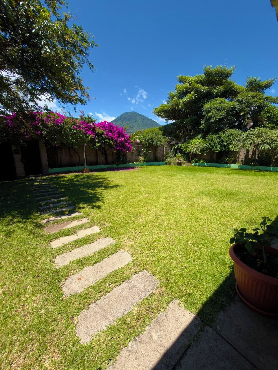 A well-maintained grassy area with stepping stones leading to a building entrance, surrounded by lush greenery and a mountain in the background.
