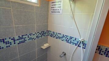 Ducha con cabezal de ducha manual, suelo de baldosas y un letrero que indica abrir primero la puerta del baño.