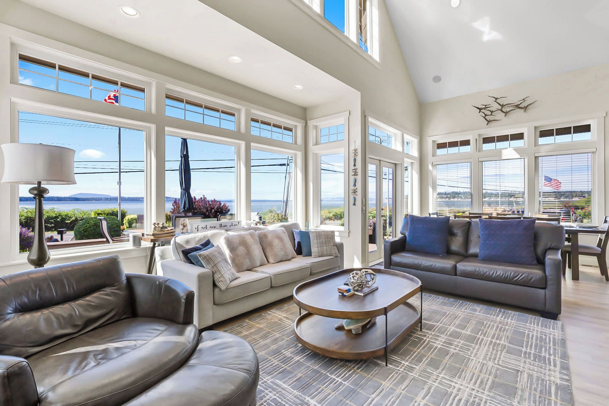 A spacious living room with large windows, a high ceiling, and a view of the outdoors.
