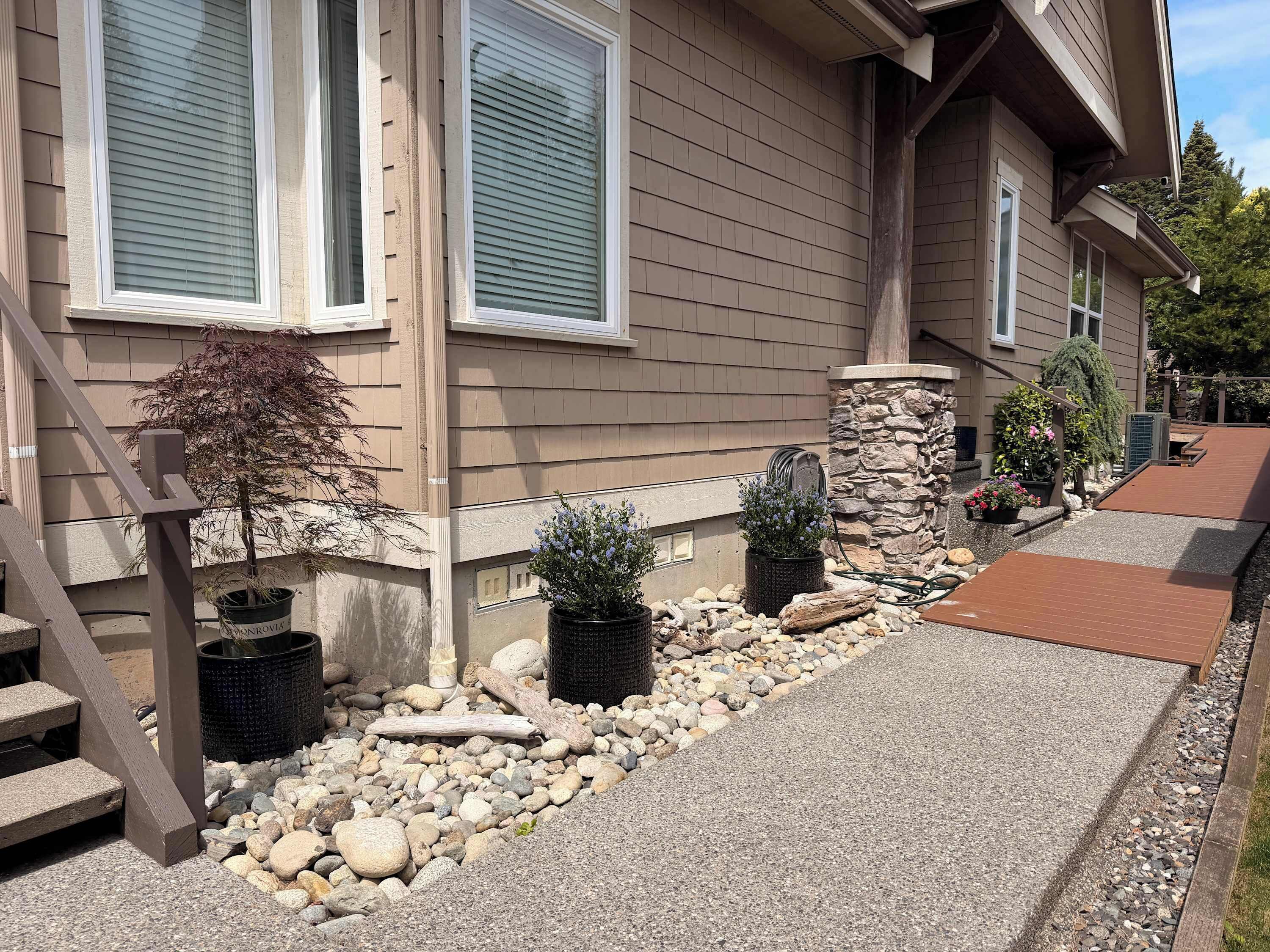A residential building with a stone foundation, a wooden deck, and potted plants.