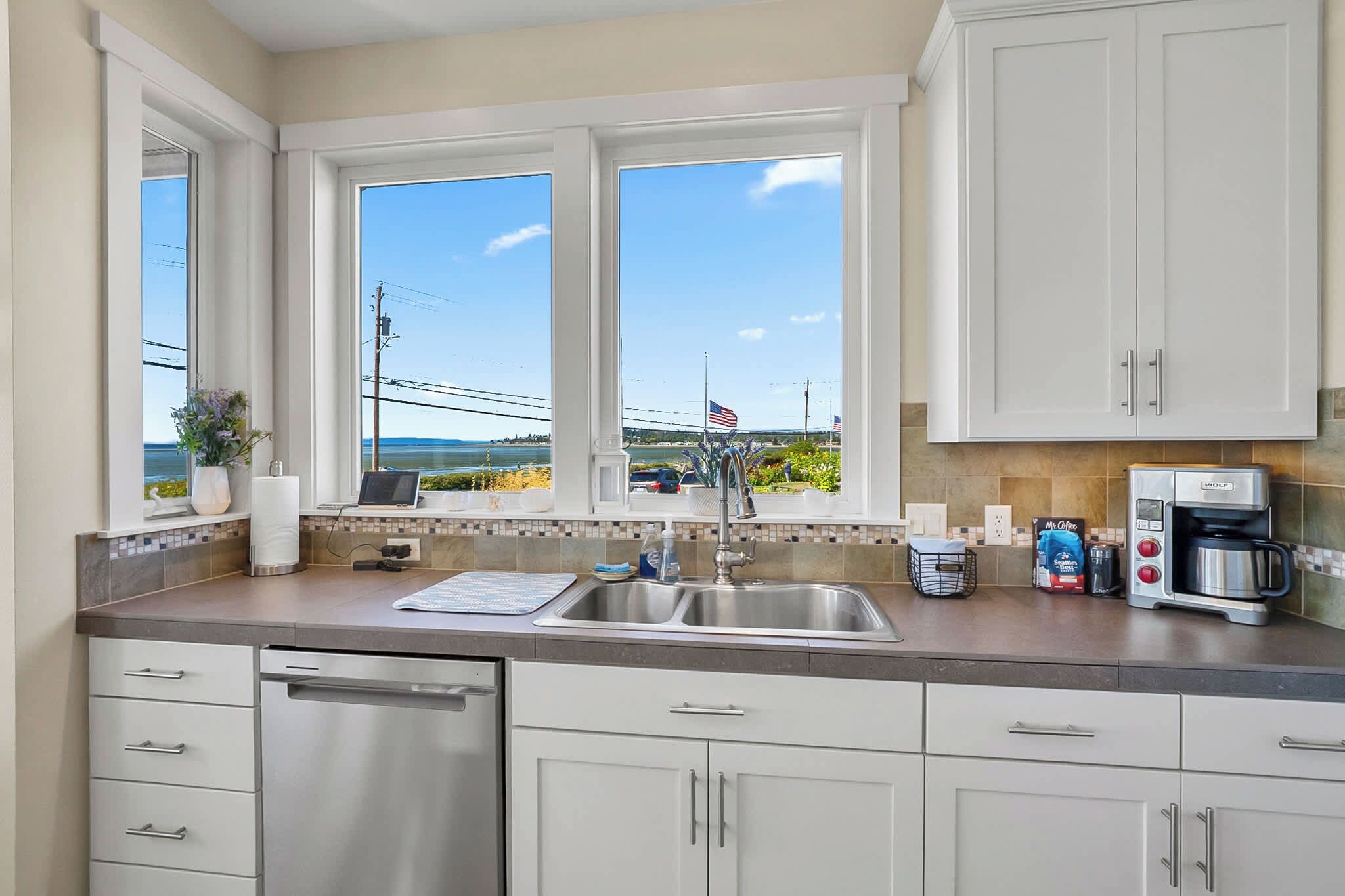Una cocina con un lavamanos de acero inoxidable, armarios blancos y vistas al océano.