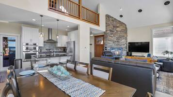 Una cocina moderna con electrodomésticos de acero inoxidable, un comedor con mesa de madera y un tazón decorativo azul, y una chimenea de piedra en la sala de estar.