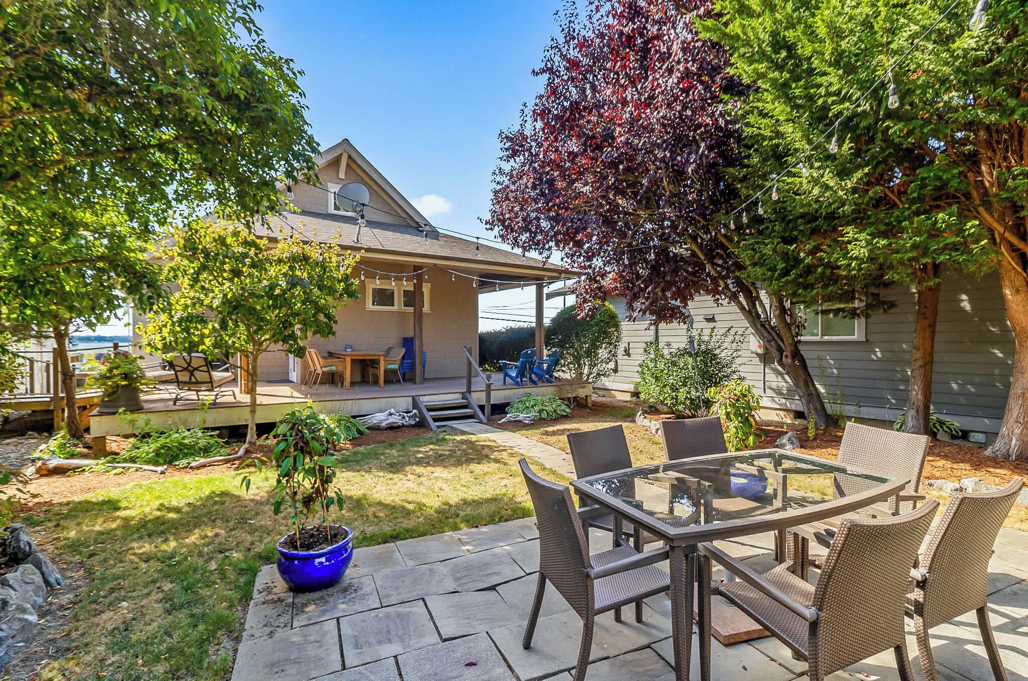 A patio area with a glass-top table and wicker chairs, surrounded by a well-maintained lawn and a house in the background.