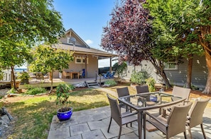 A patio area with a glass-top table and wicker chairs, surrounded by a well-maintained lawn and a house in the background.