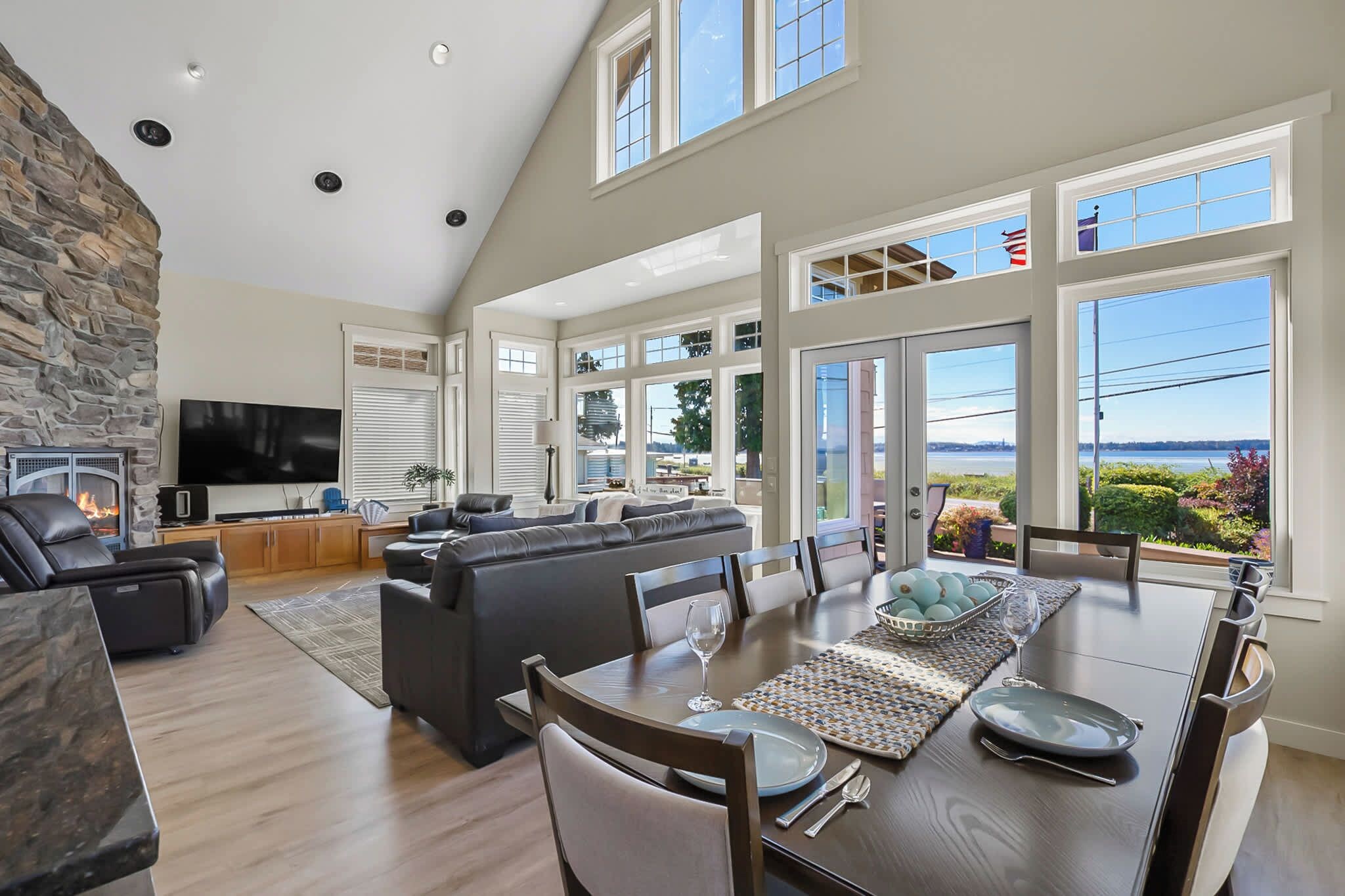 A spacious living room with a stone fireplace, a flat-screen TV, and a large window overlooking a scenic view.
