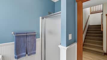 Une salle de bain dotée d’une porte de douche en verre, d’un porte-serviettes avec deux serviettes et d’un escalier en bois menant à l’étage supérieur.
