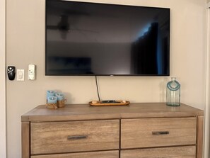 A flat-screen TV mounted on a wall above a wooden dresser with drawers and a small tray. - Upgraded 1BD/1.5BA ocean view condo steps away from fantastic Kam 1 beach (kihei)