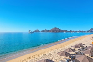Una platja amb aigua blava cristal·lina, un iaiot i una filera de sombrerelles de platja.