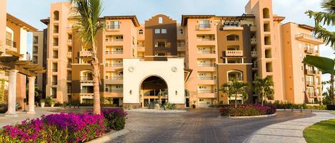 A multi-story hotel with a central entrance, balconies, and surrounding landscaping.