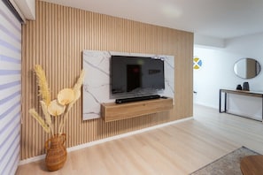 A modern living room with a flat-screen TV mounted on a wooden wall, a console table, and a vase with dried plants.