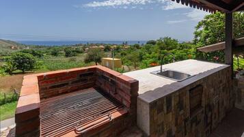 A brick barbecue grill with a sink on a patio overlooking a scenic landscape.