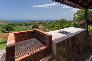 A brick barbecue grill with a sink on a patio overlooking a scenic landscape.