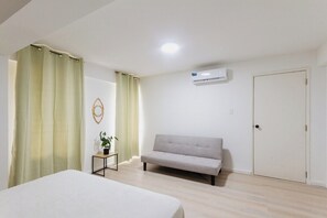 A bedroom with a bed, a sofa, a small table with a plant, and a door.
