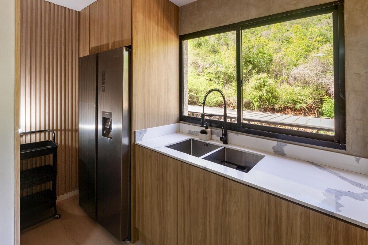 Una cocina moderna con un refrigerador de acero inoxidable, un lavamanos doble y un ventanal con vista a follaje.