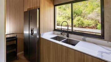 A modern kitchen with a stainless steel refrigerator, a double sink, and a window with a view of greenery.