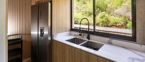 Una cocina moderna con un refrigerador de acero inoxidable, un lavamanos doble y un ventanal con vista a follaje.