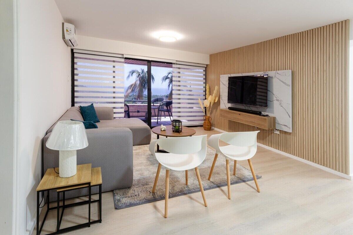 Ein modernes Wohnzimmer mit einer Couch, einem Couchtisch und zwei Sesseln. An der Wand ist ein Flachbildfernseher angebracht.