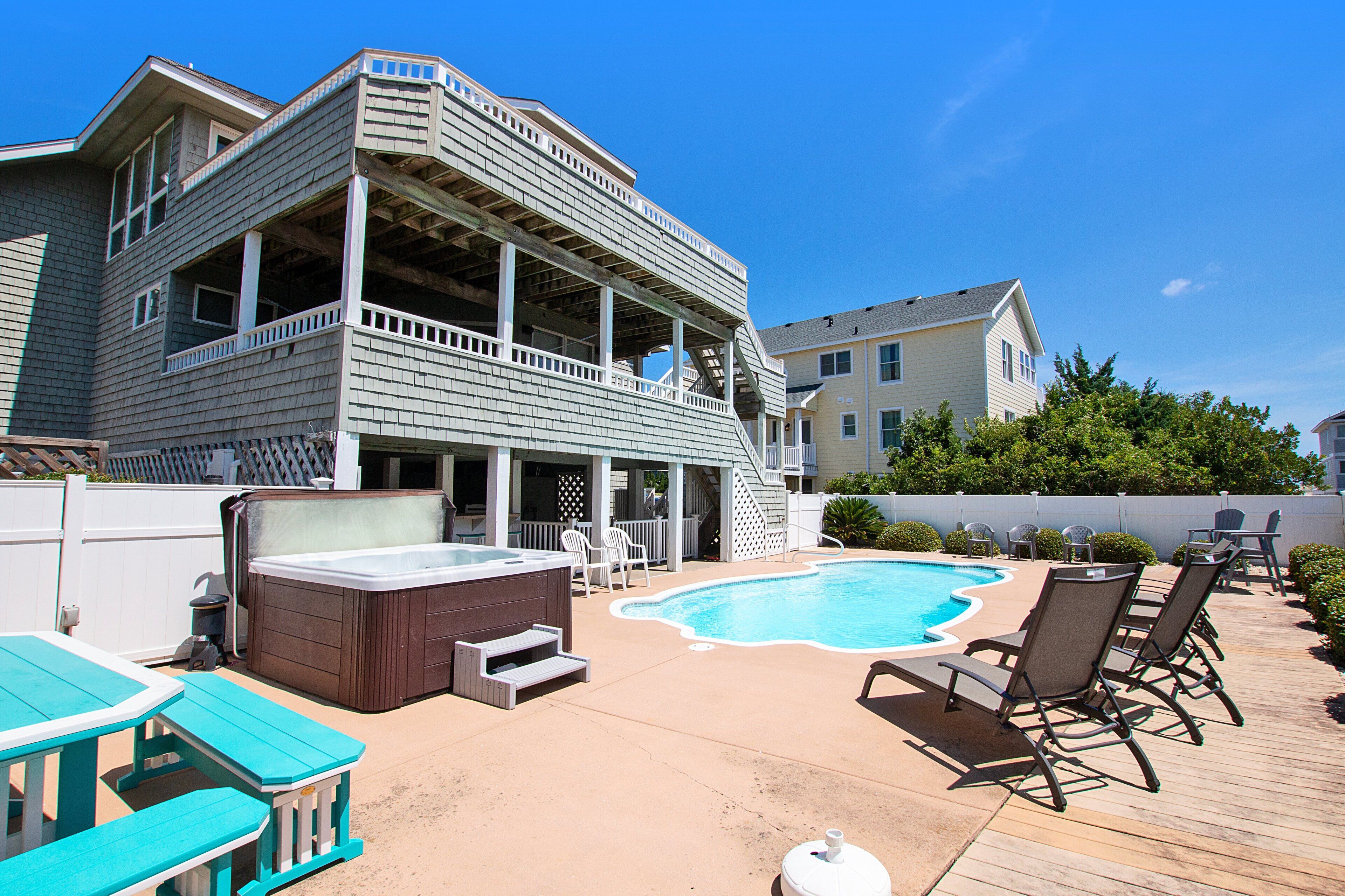 A two-story house with a backyard featuring a swimming pool, lounge chairs, and a hot tub.