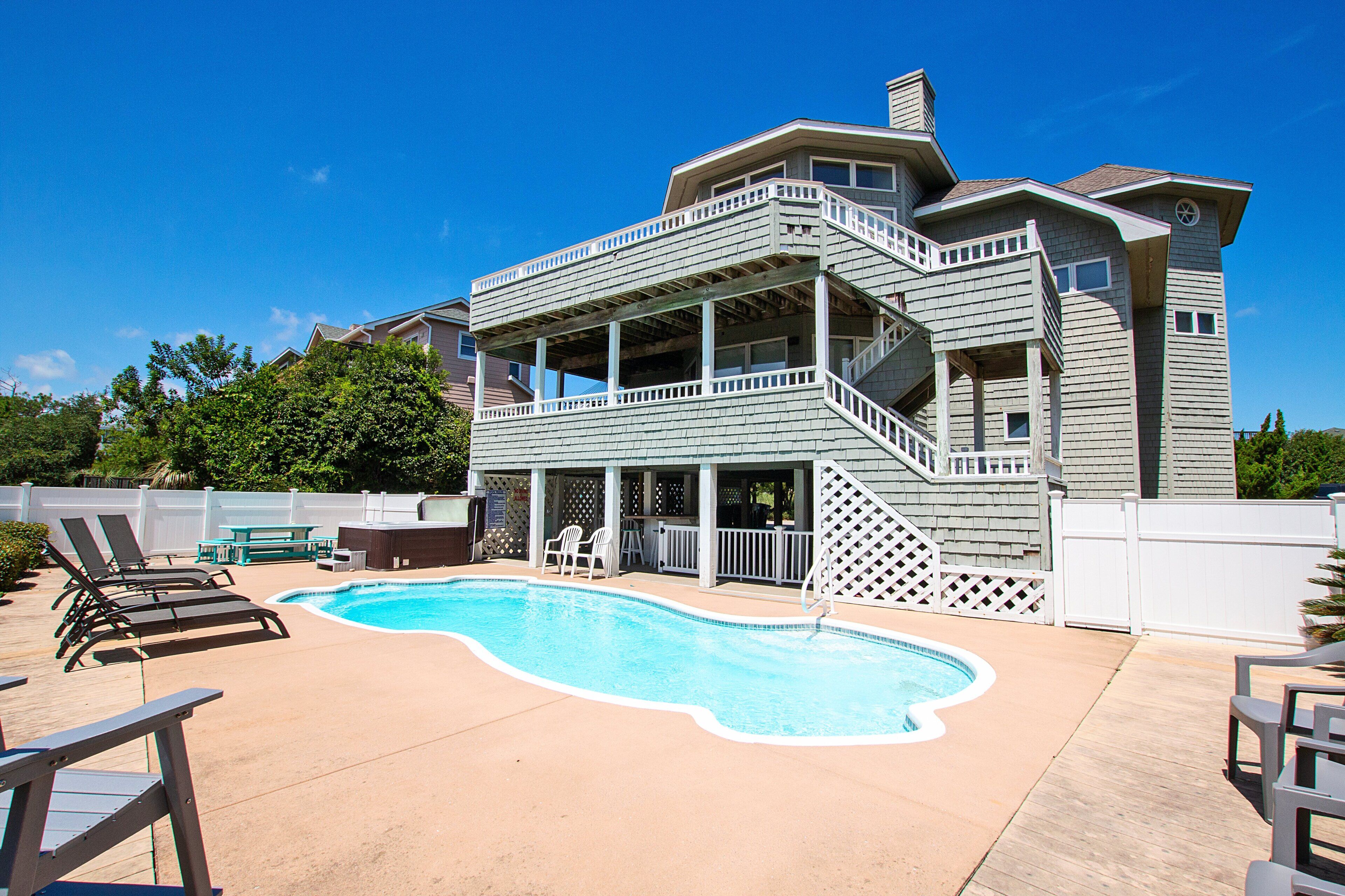 Une maison à deux étages avec une piscine, du mobilier d’extérieur et un patio couvert.