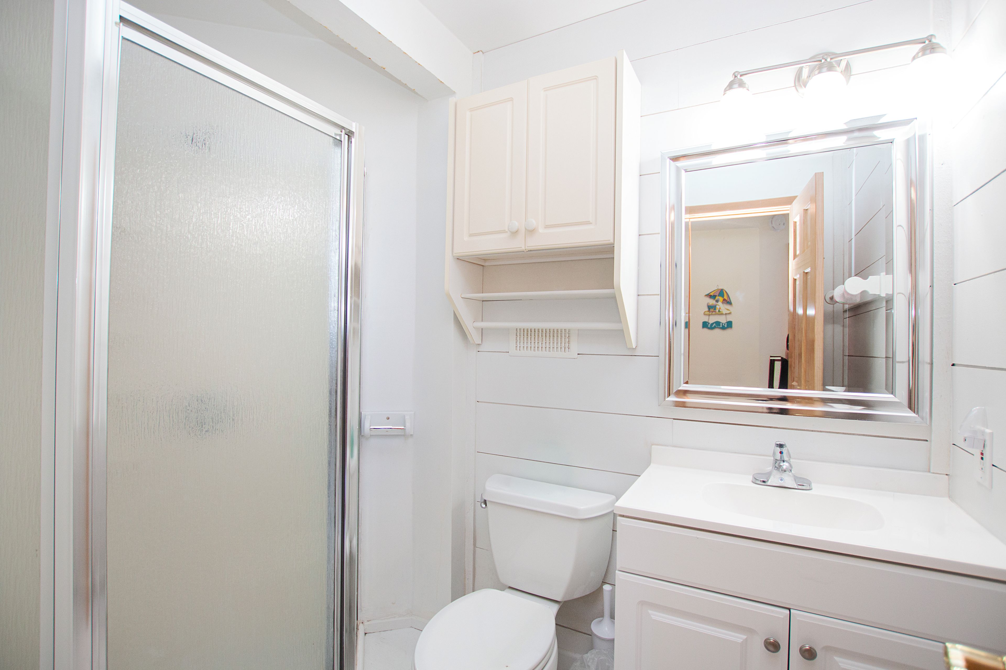 A bathroom with a toilet, a sink, a mirror, and a cabinet.