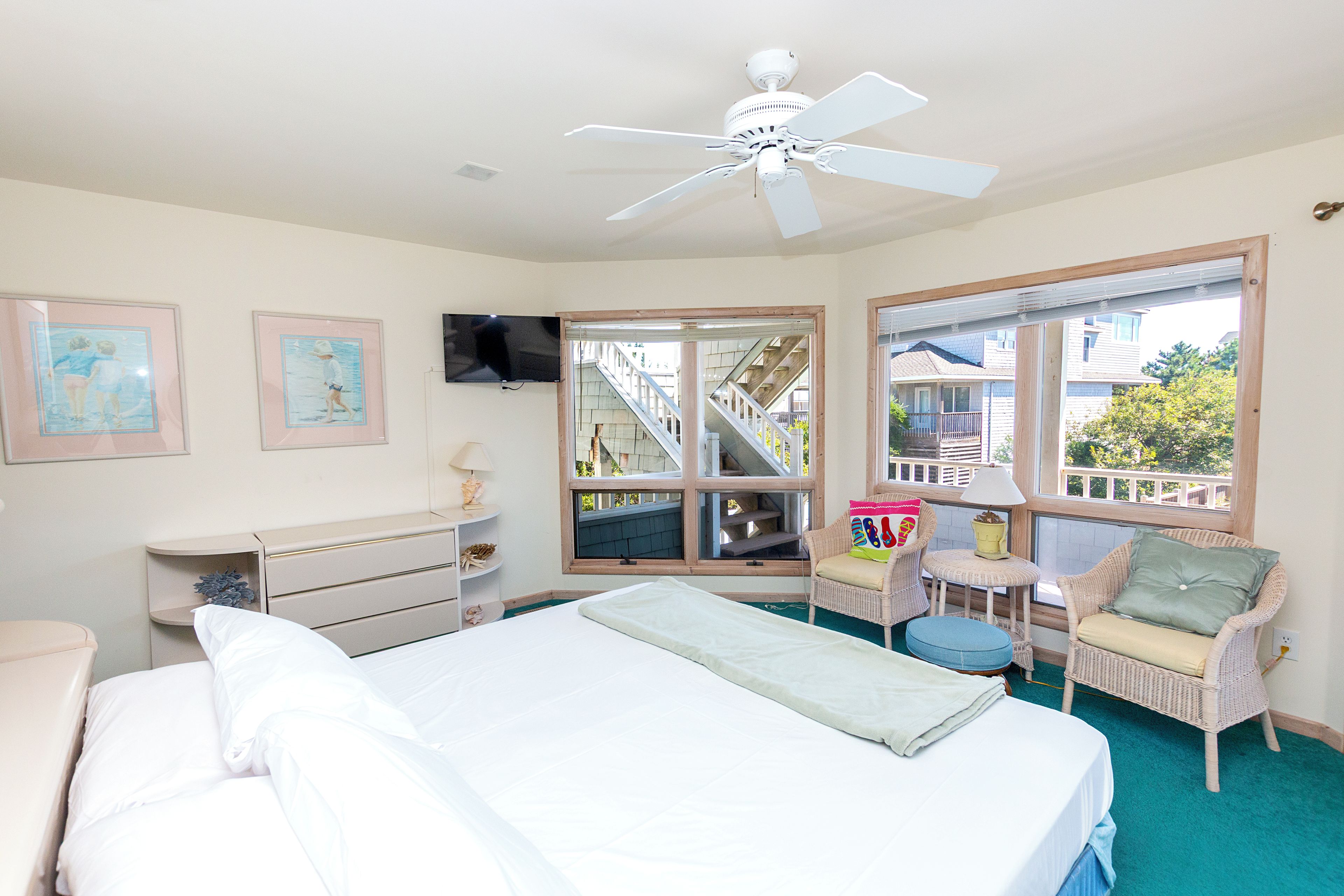 A bedroom with a bed, a desk, a chair, a window with a view of a staircase, and a ceiling fan.