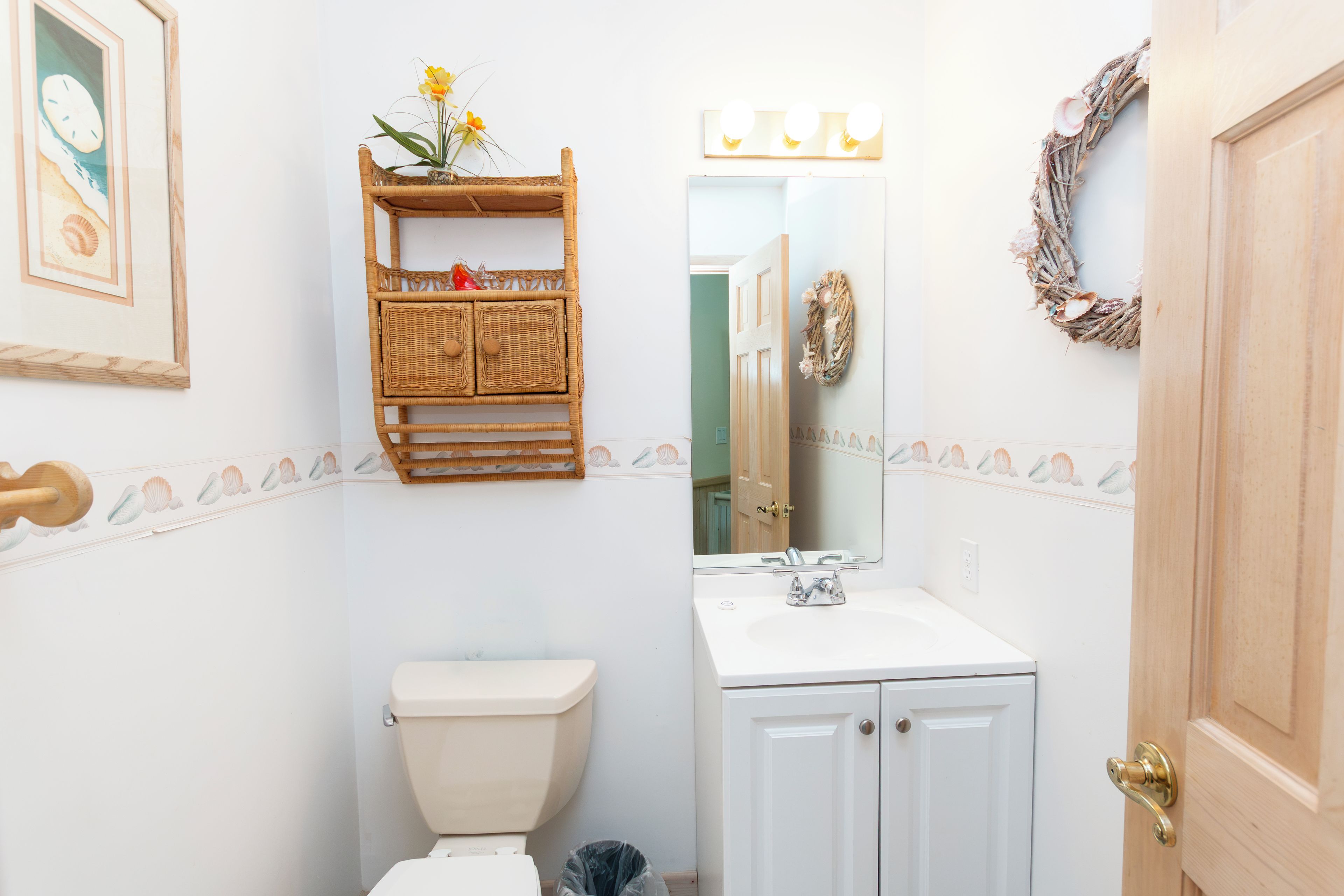 A bathroom with a toilet, a vanity with a mirror, and a shelf above the toilet.