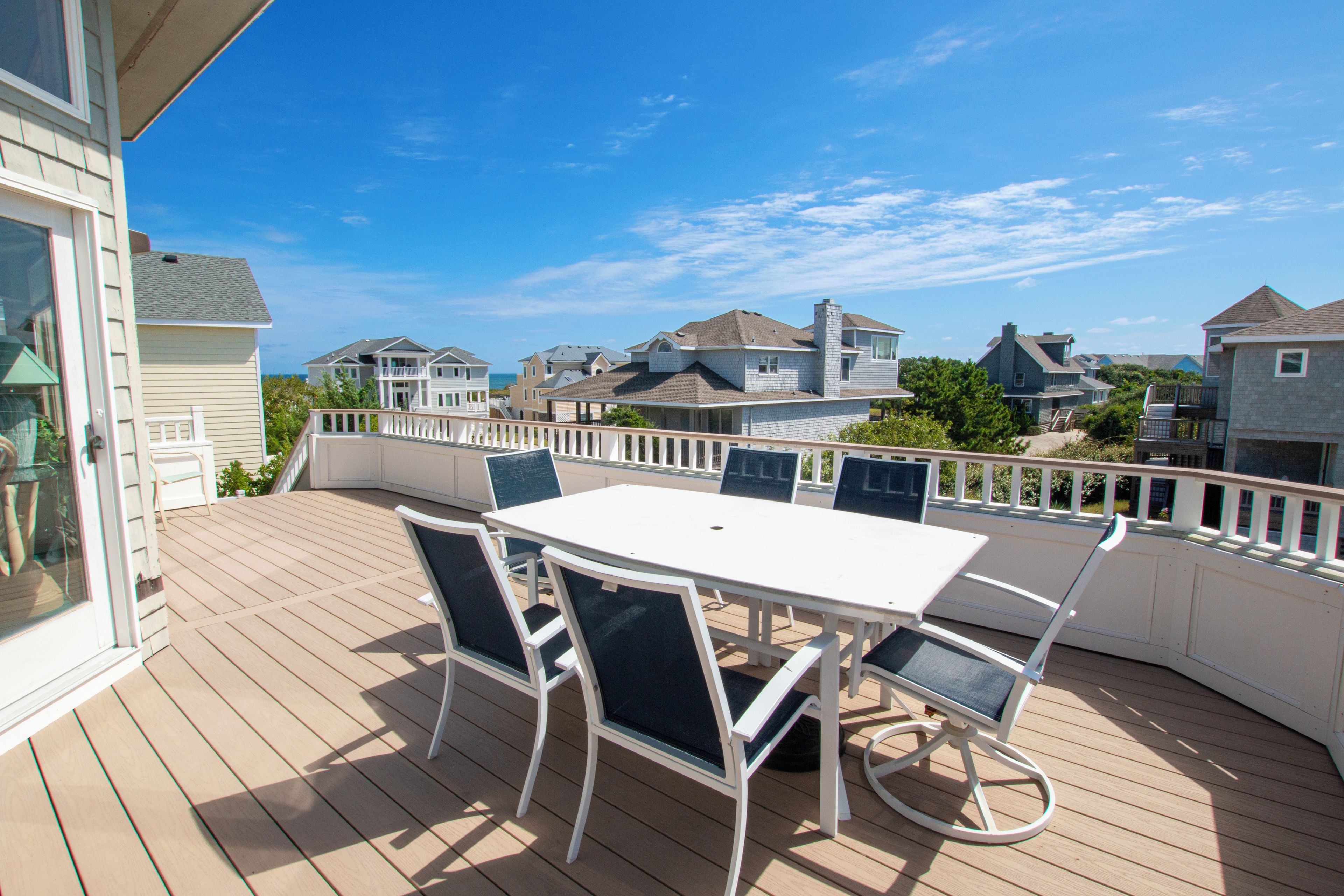 A deck with a white table and chairs, overlooking a residential area with houses and a clear sky.