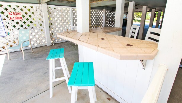 A covered outdoor area with a white wooden bar and two turquoise stools. - Oceanside-Priv Pool, Htub, Resort Access -133, I SEA the Light (Corolla)