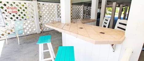 A covered outdoor area with a white wooden bar and two turquoise stools.