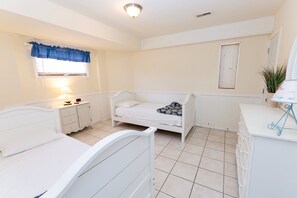 A bedroom with two beds, a bedside table with a lamp, a window with a curtain, a door, and a small plant on a table. - OCEANFRONT, Ocean views, Dogs Welcome, Hot Tub- CP24, ROAR by the Shore (Corolla)