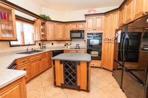 A kitchen with wooden cabinets, a central island, stainless steel appliances, and a window with curtains. - OCEANFRONT, Ocean views, Dogs Welcome, Hot Tub- CP24, ROAR by the Shore (Corolla)