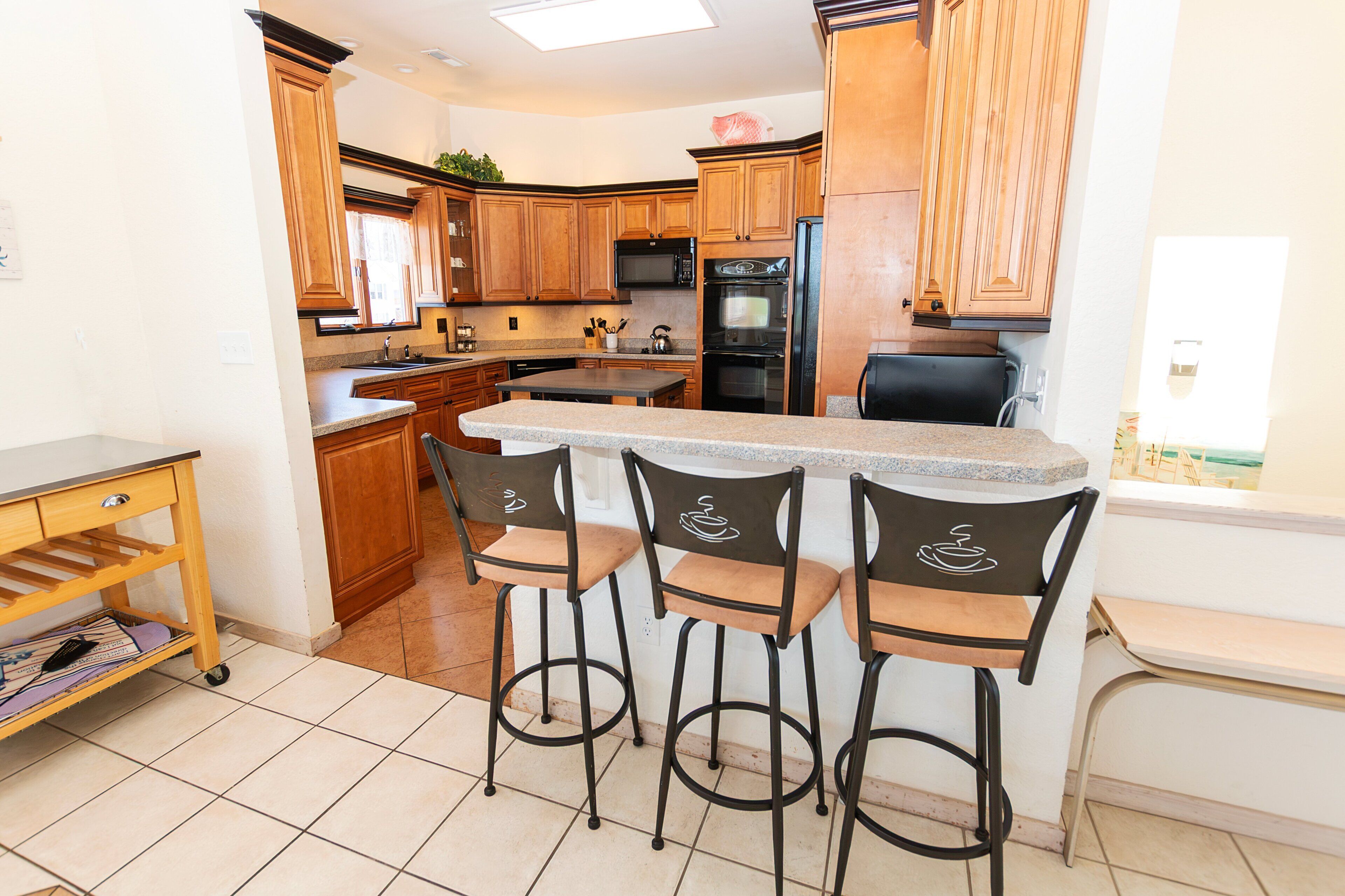 A kitchen with wooden cabinets, a central island with bar stools, a microwave, and an oven.