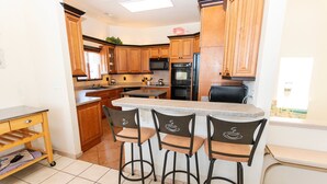 A kitchen with wooden cabinets, a central island with bar stools, a microwave, and an oven. - OCEANFRONT, Ocean views, Dogs Welcome, Hot Tub- CP24, ROAR by the Shore (Corolla)