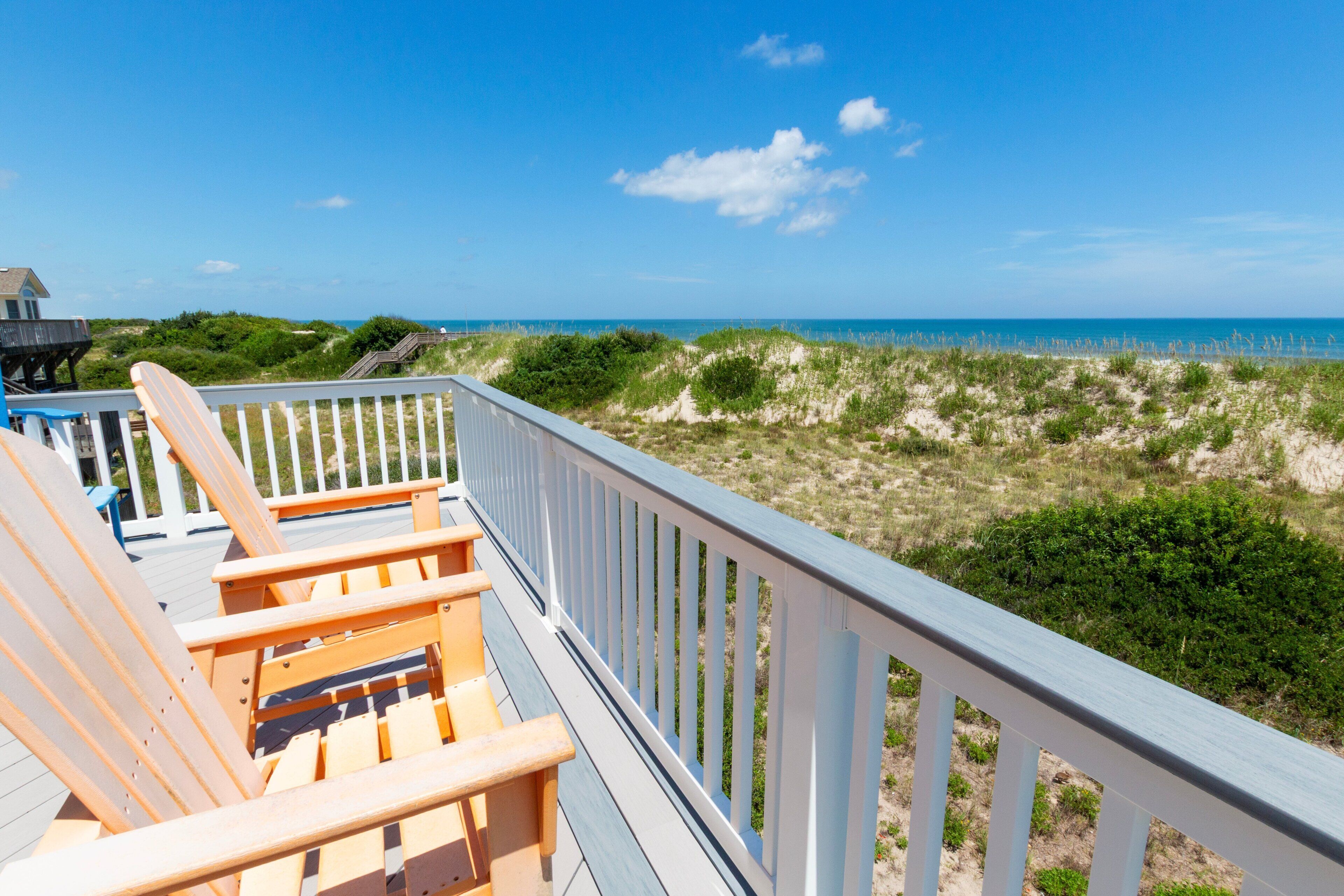 A wooden deck with chairs overlooking a beach and dunes.