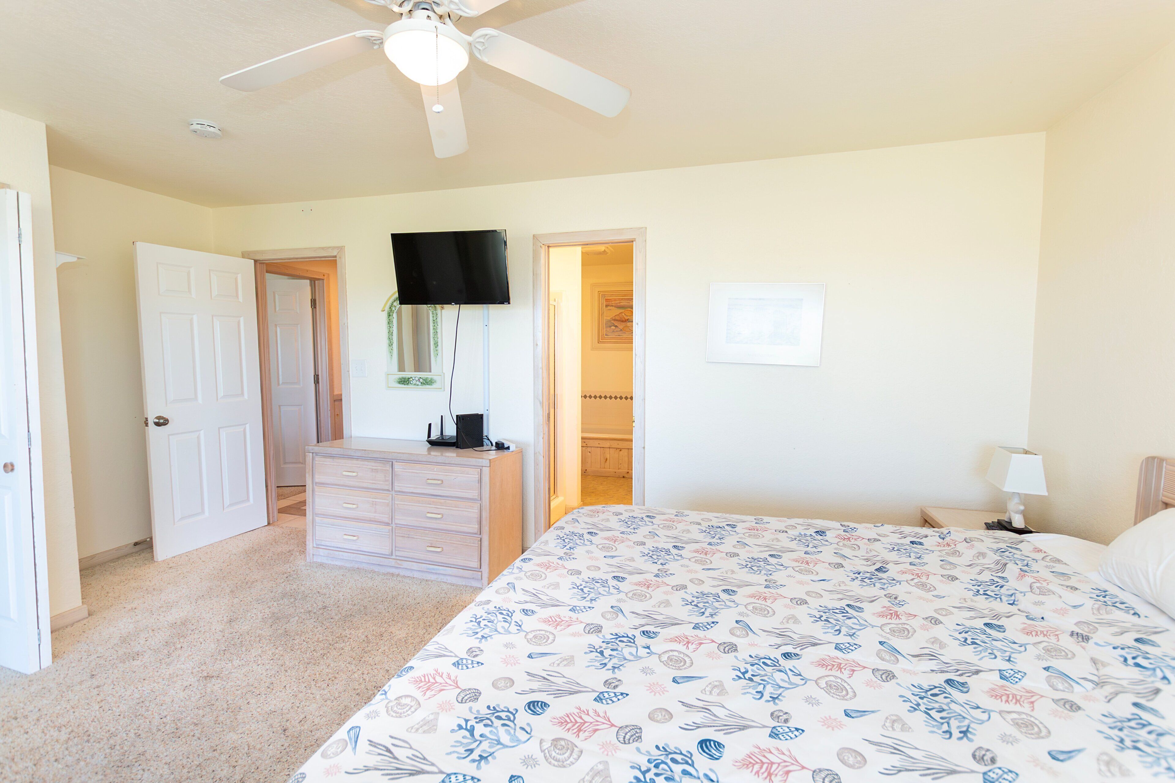 A bedroom with a bed, dresser, TV, and a ceiling fan.