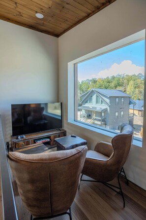 A modern living room with a large window, a flat-screen TV, and two leather chairs. - 2 Cabins - Indoor Pool & 2 Hot Tubs - Sleeps 13 (Pigeon Forge)