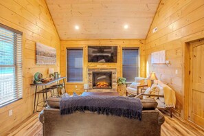 Ein Blockhaussalon mit Kamin, Holzwänden, einer Couch und einem Esstisch.