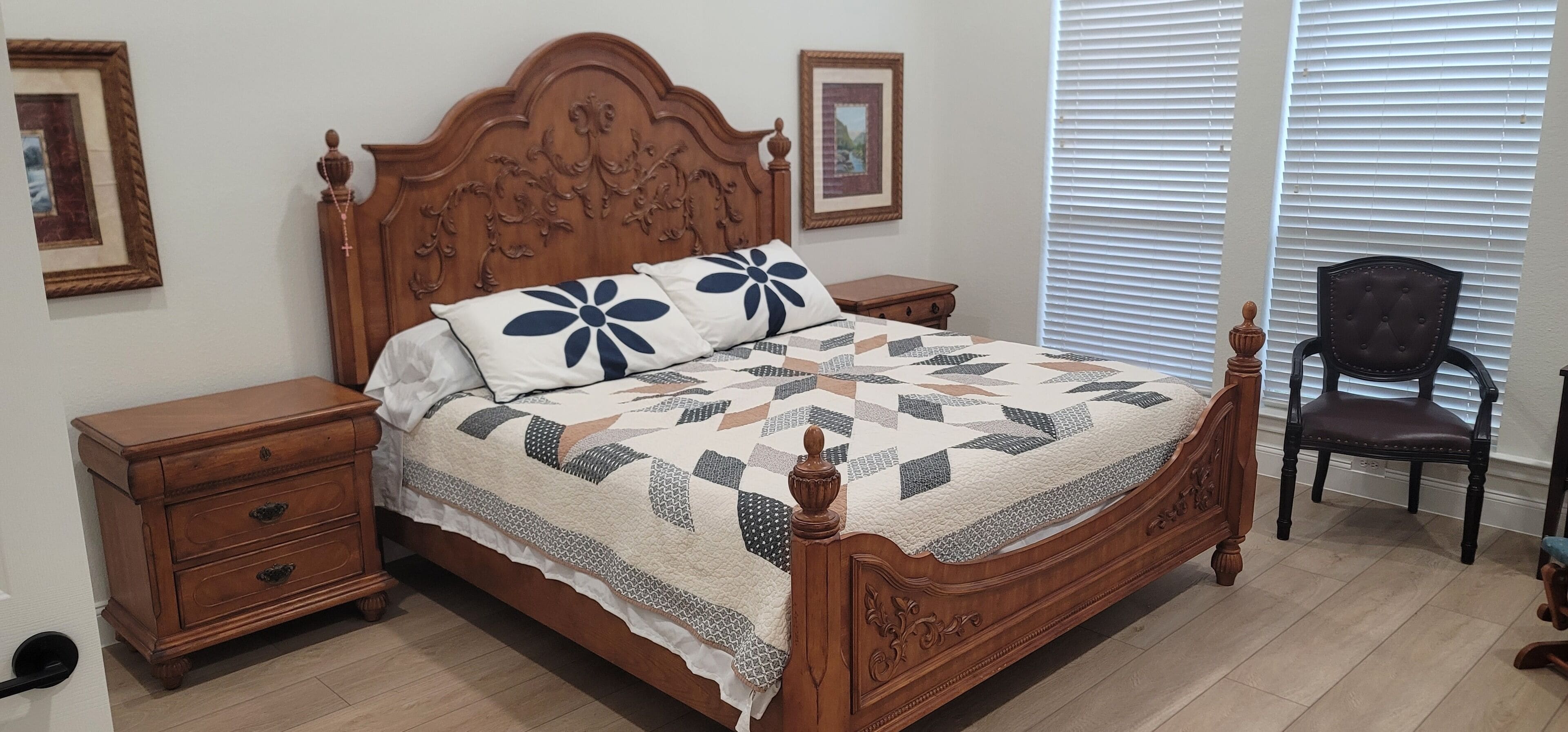 Una cama con dosel de madera, con colcha, dos mesitas de noche, una silla y cuadros enmarcados en las paredes.