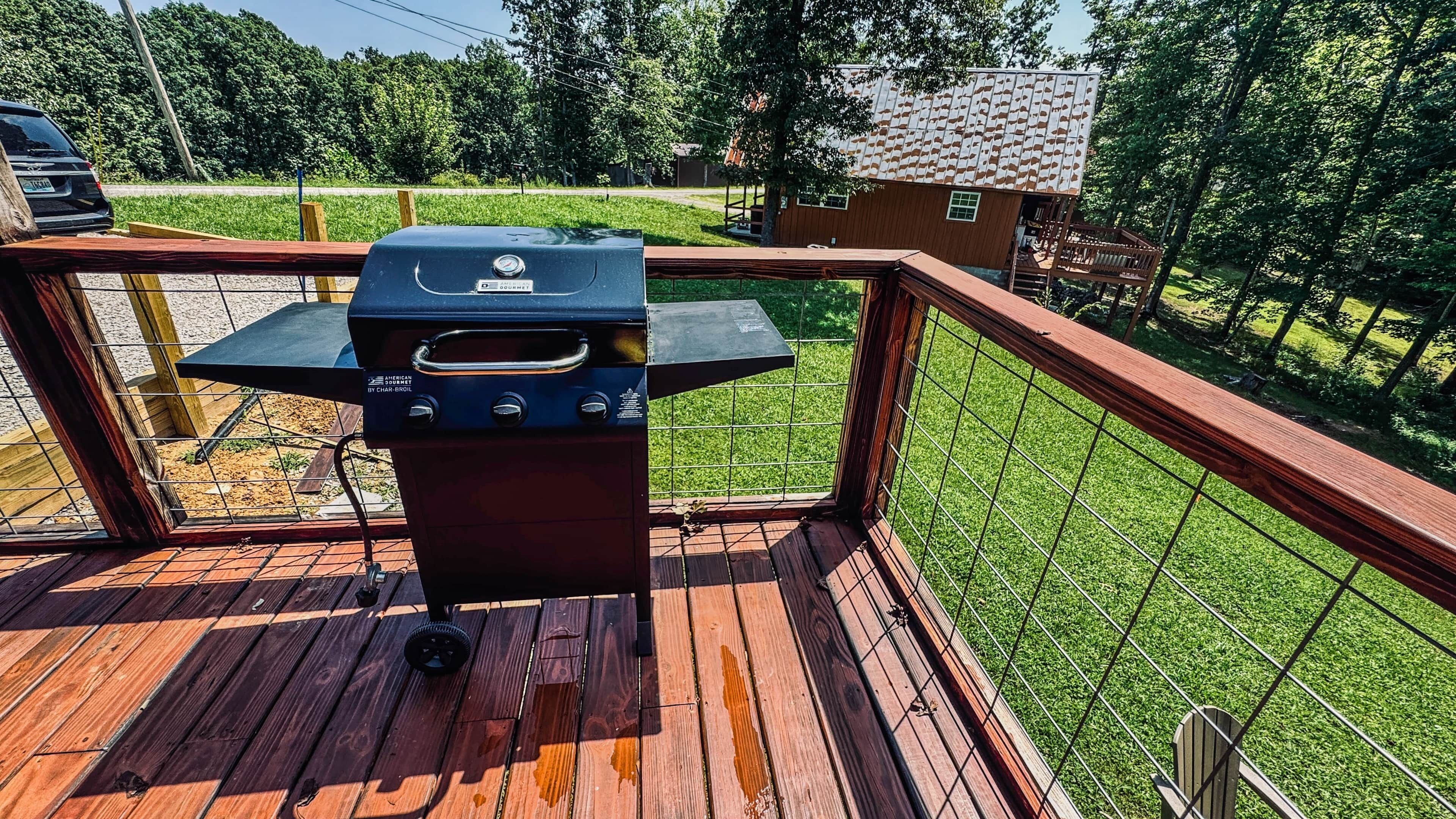 Una parrilla de barbacoa en una terraza de madera, con vista a un jardín césped y una casa al fondo.