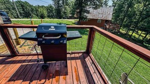 A barbecue grill on a wooden deck with a view of a grassy yard and a house in the background.