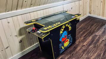 A small arcade machine with a colorful design, placed in a corner with wooden walls and flooring.