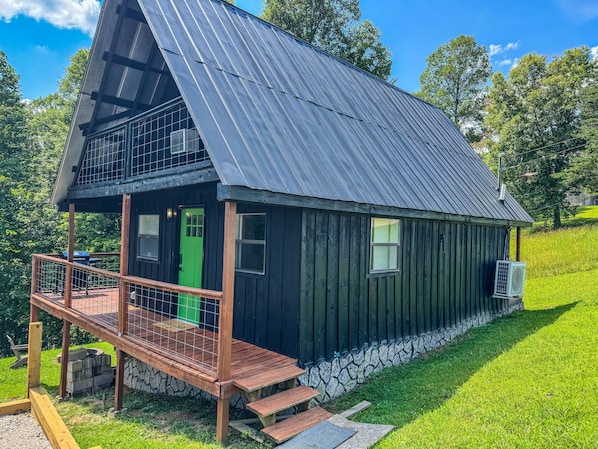 A two-story cabin with a metal roof, a green door, and a wooden deck.