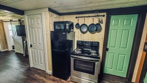 A kitchen with a black refrigerator, a stove, and a microwave. There are wooden cabinets and a green door.