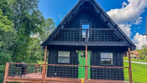 A two-story wooden cabin with a green door, a balcony with a railing, and a stone foundation.