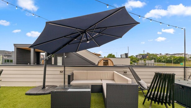 Un espacio al aire libre con sillones, un sofá y una mesa, todo cubierto por un gran paraguas.