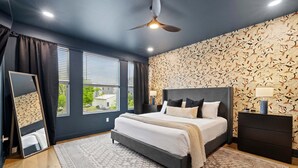 Un dormitorio moderno con una cama grande, ventilador de techo, mesita de noche y un papel tapiz con diseño.