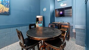 Una habitación con una mesa redonda, sillas, un televisor y una consola de videojuegos.