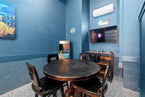Ein Zimmer mit einem runden Tisch, Stühlen, einem Fernseher und einer Spielkonsole.