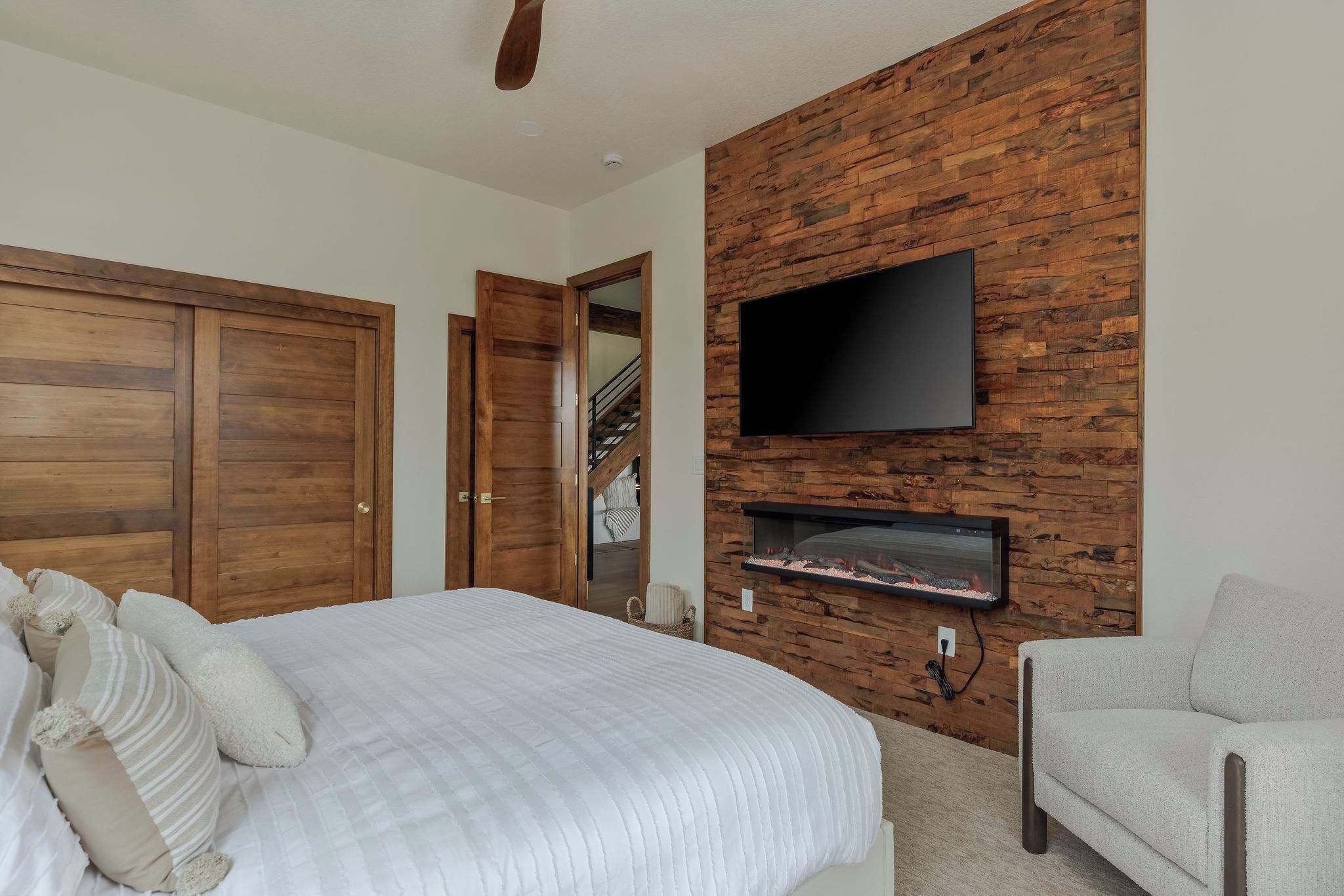 Un dormitorio con una cama grande, un televisor montado en una pared de madera y una chimenea.