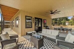 Ein Terrassenbereich im Freien mit Korbmöbeln, einem Glastisch und einem Deckenventilator.